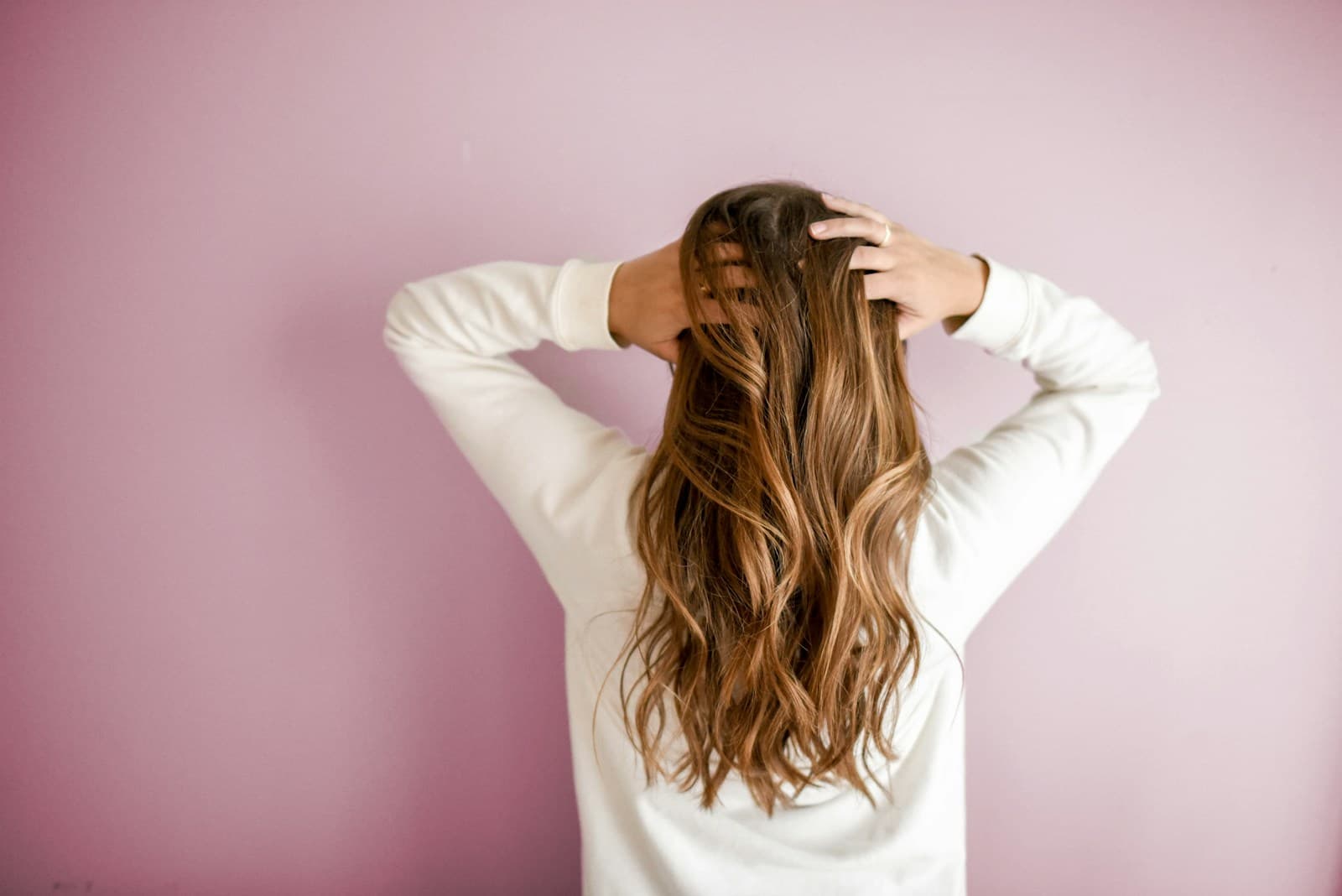Woman with long hair photographed from behind against a pink wall